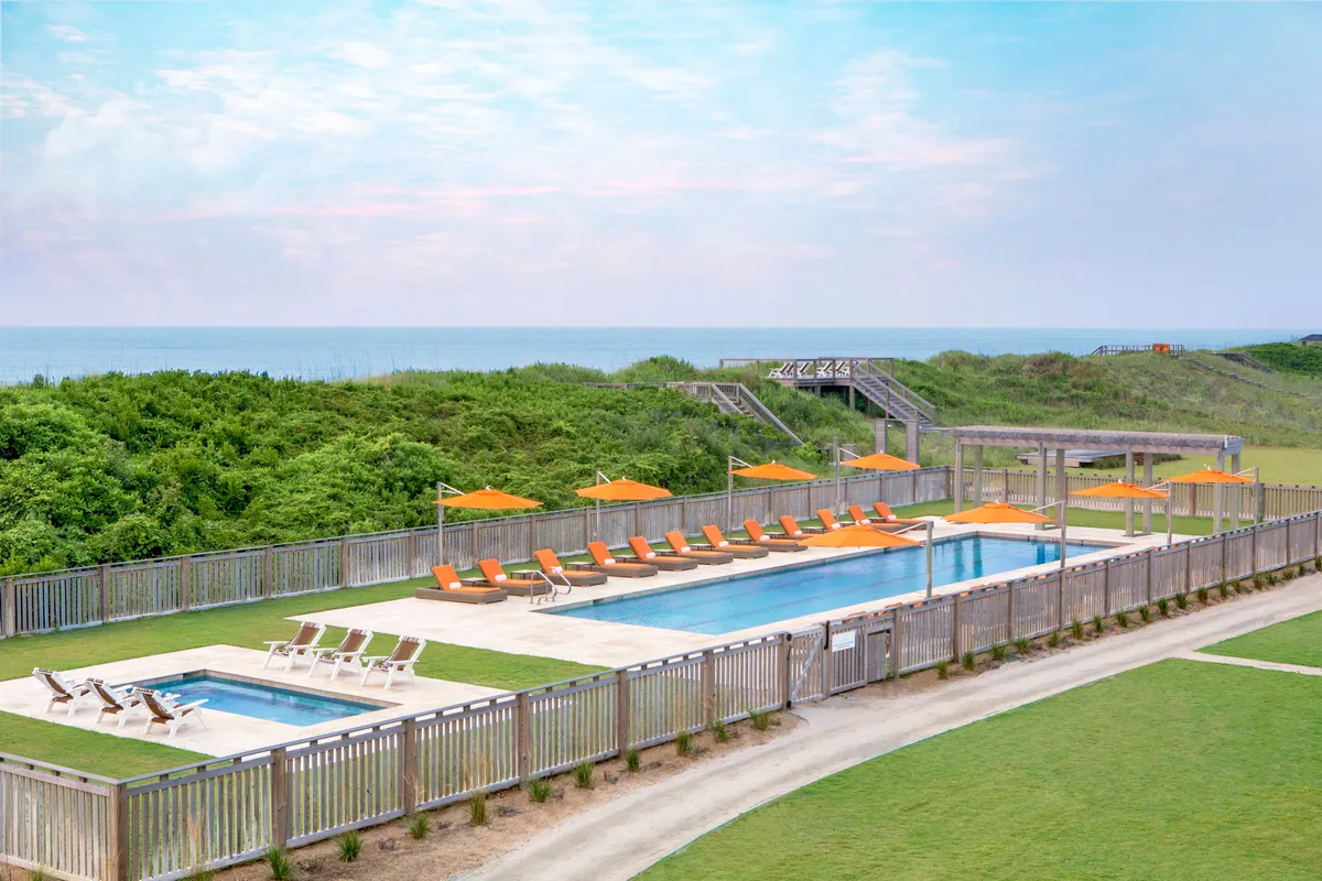 An inviting exterior shot of the resort's swimming pool surrounded by lounge chairs and orange umbrellas, with lush greenery in the background. The area is bathed in warm light, suggesting sunset or early evening—times ideal for relaxation and intimate moments by the pool.
