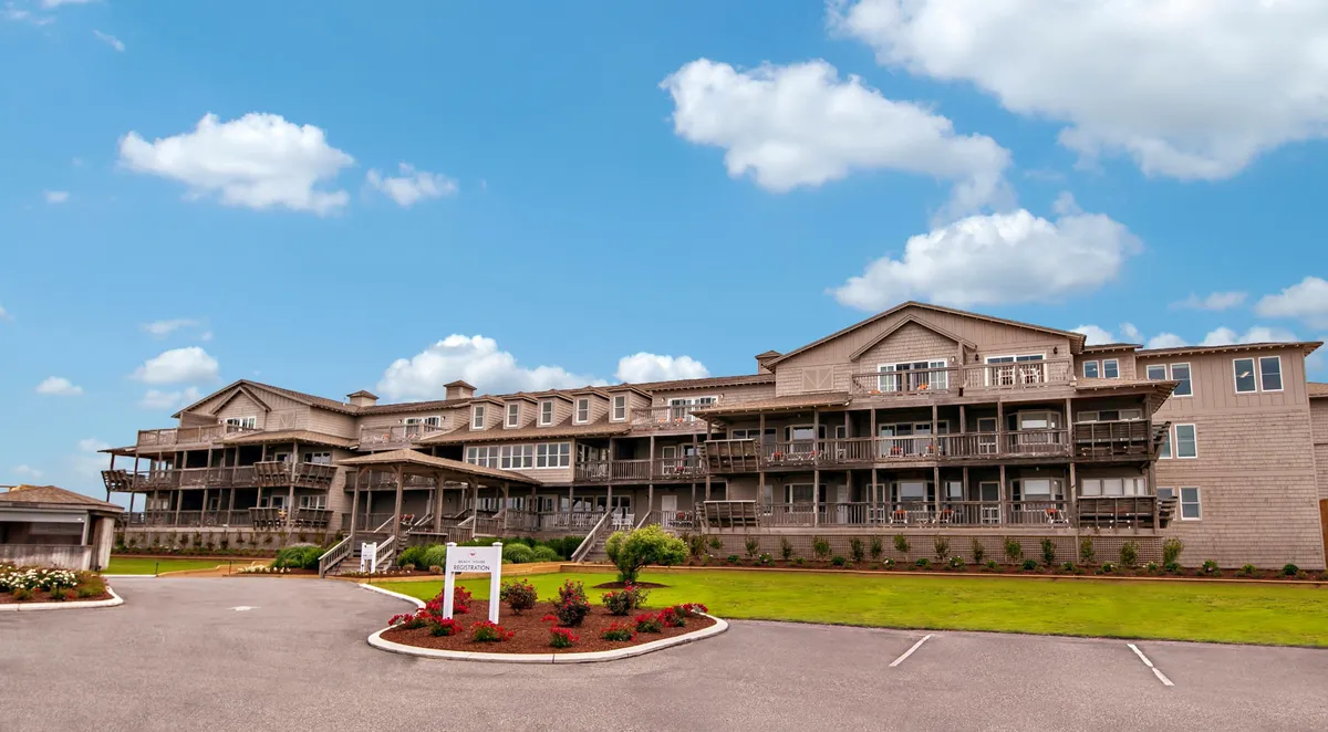 A multi-story building featuring prominent private balconies with glass railings, surrounded by a landscaped garden. Several balconies are visible, suggesting inviting outdoor spaces with ample room for seating and relaxation. The setting sun casts a warm glow, hinting at the potential for beautiful sunset views from the balconies.