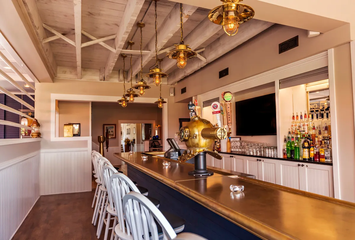 An interior scene of the resort’s bar area, with a stylish counter, hanging lights, and decorative elements. The mood is casual and sociable, with hints of activity like socializing and relaxing, aligning with the resort’s offering of nourishing meals and communal spaces.