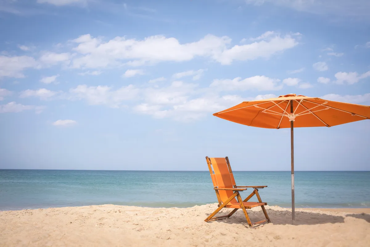This image captures a tranquil stretch of private beach, featuring orange chairs and umbrellas set on the sand, with the beautiful ocean water in the background. The scene radiates relaxation and intimacy, suggesting early morning or late afternoon light ideal for romantic walks or unwinding together by the sea.